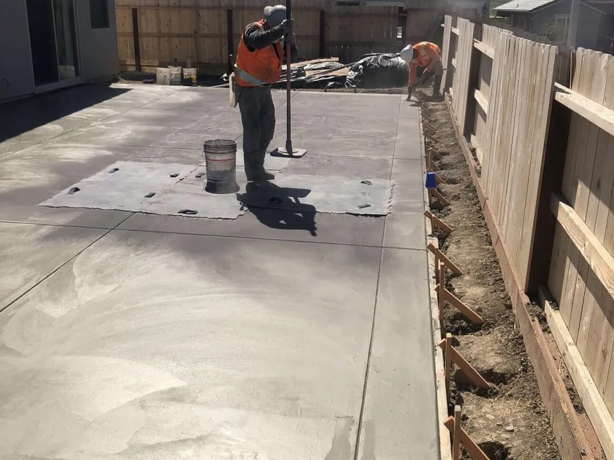 Worker floating a freshly poured backyard slab between a house and fence