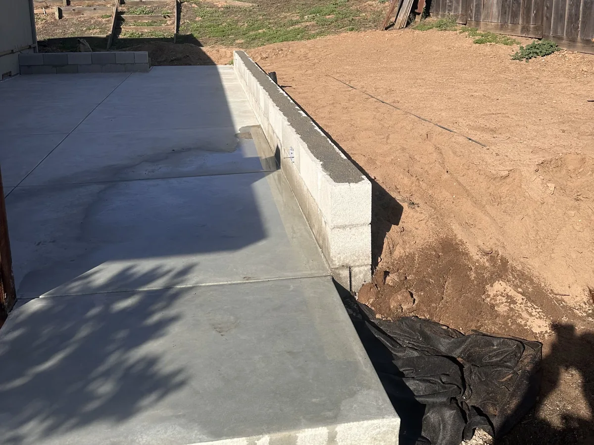 New concrete slab poured against a block retaining wall in a dirt yard