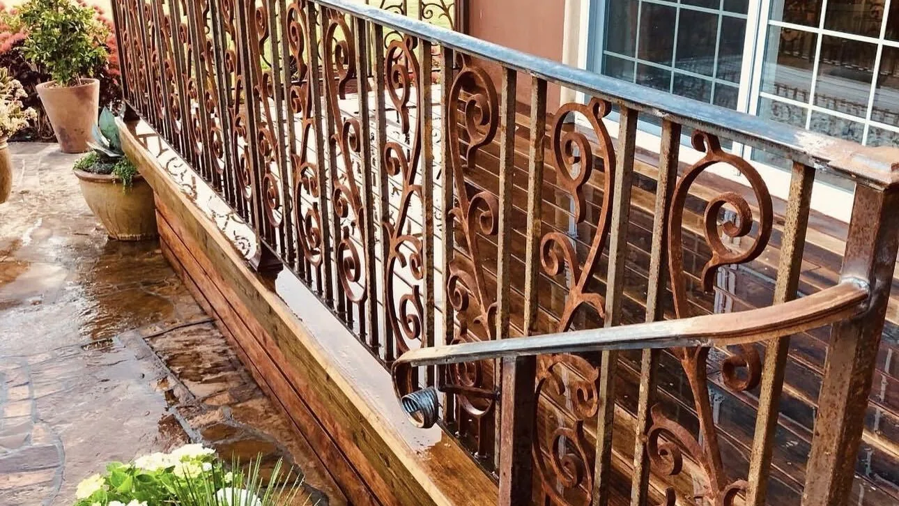 Scrolled iron railing along a deck above a rain-wet flagstone patio