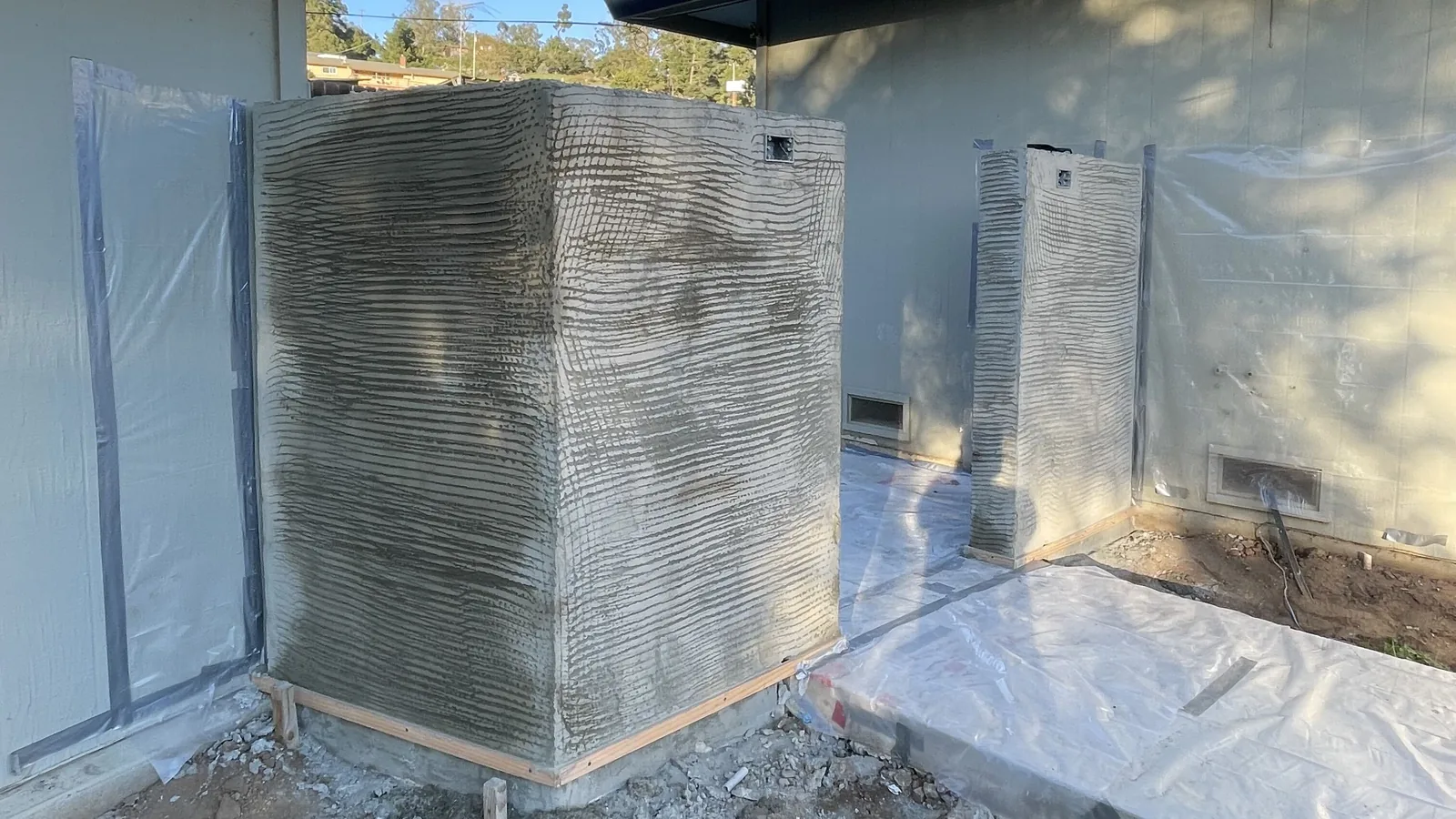 Site-built masonry columns carrying a fresh scratch coat beside a house