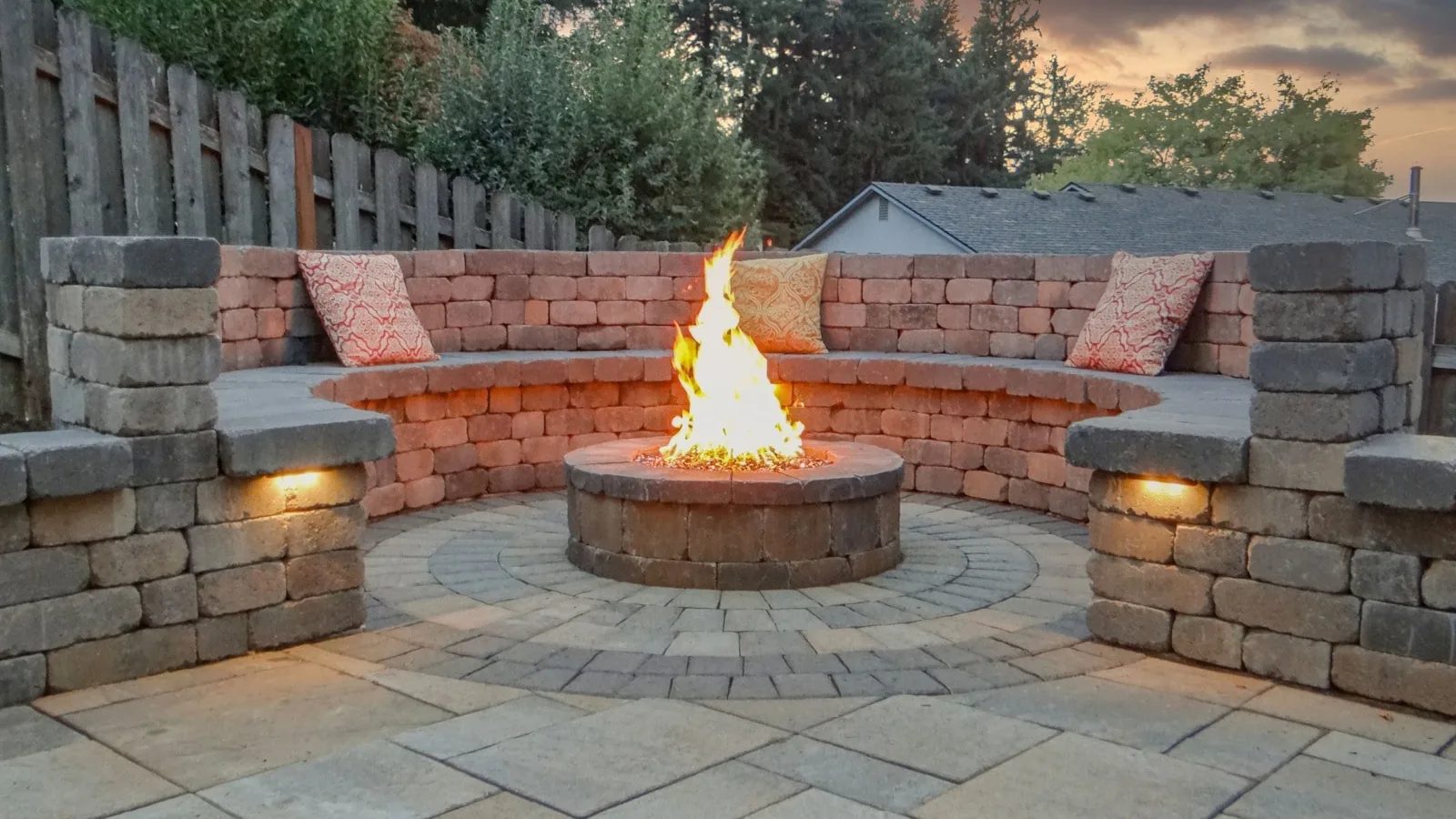 Round block fire pit burning on a paver patio with curved seat wall