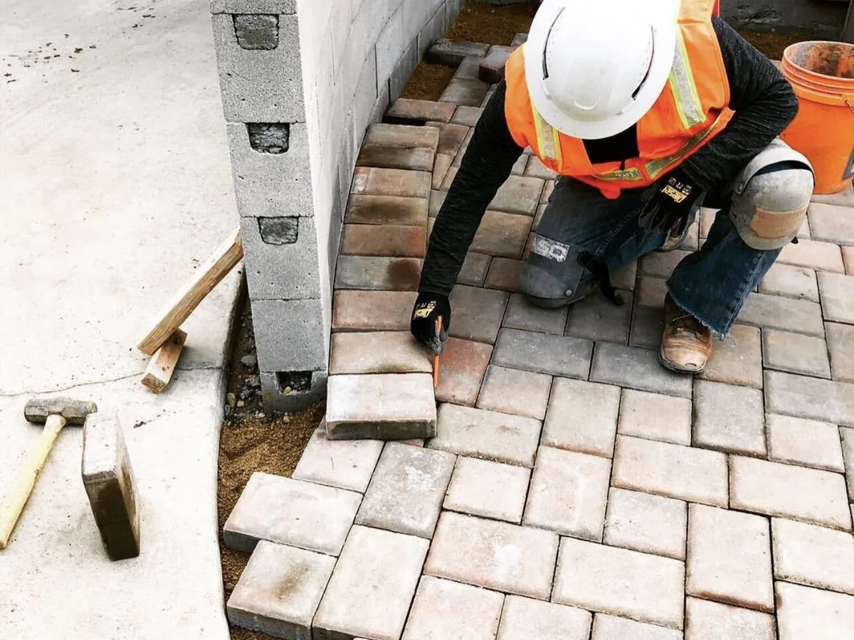 Worker in a hi-vis vest setting tumbled pavers beside a block wall