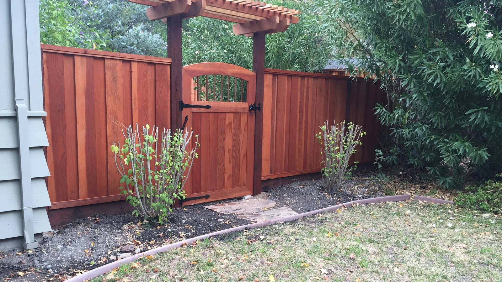 New redwood privacy fence and arched gate under a wood arbor