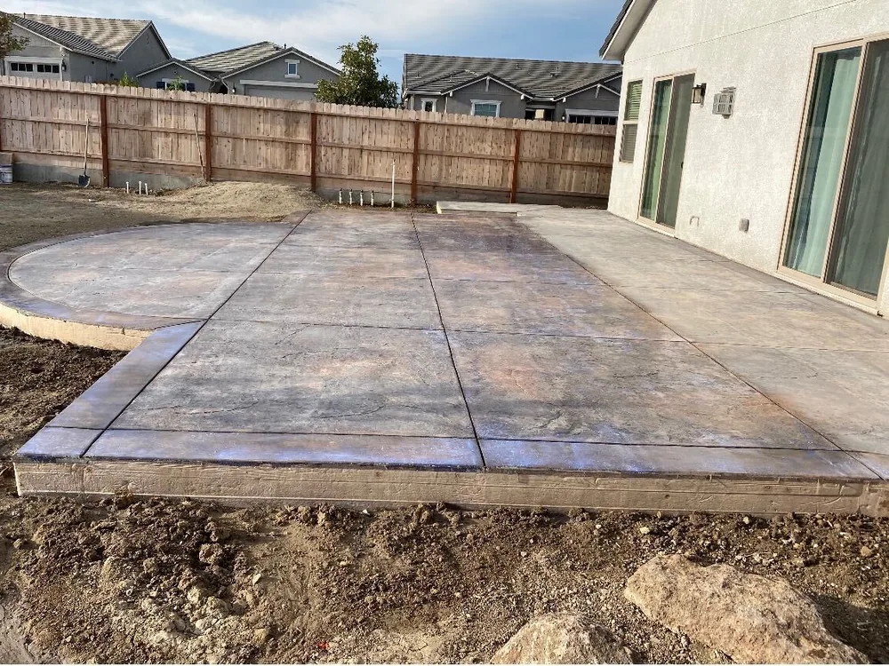 Large colored stamped patio with a curved bay beside a fenced yard